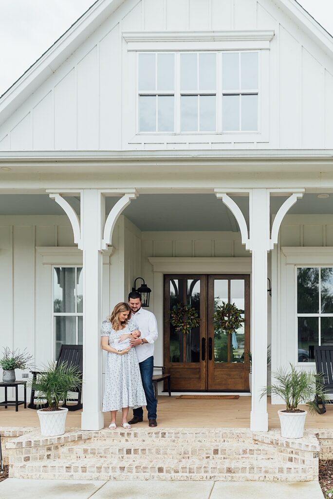Mom and dad snuggling newborn on porch