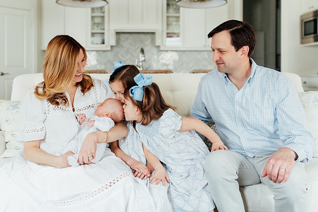 Newborn family session with sisters giving baby brother a kiss