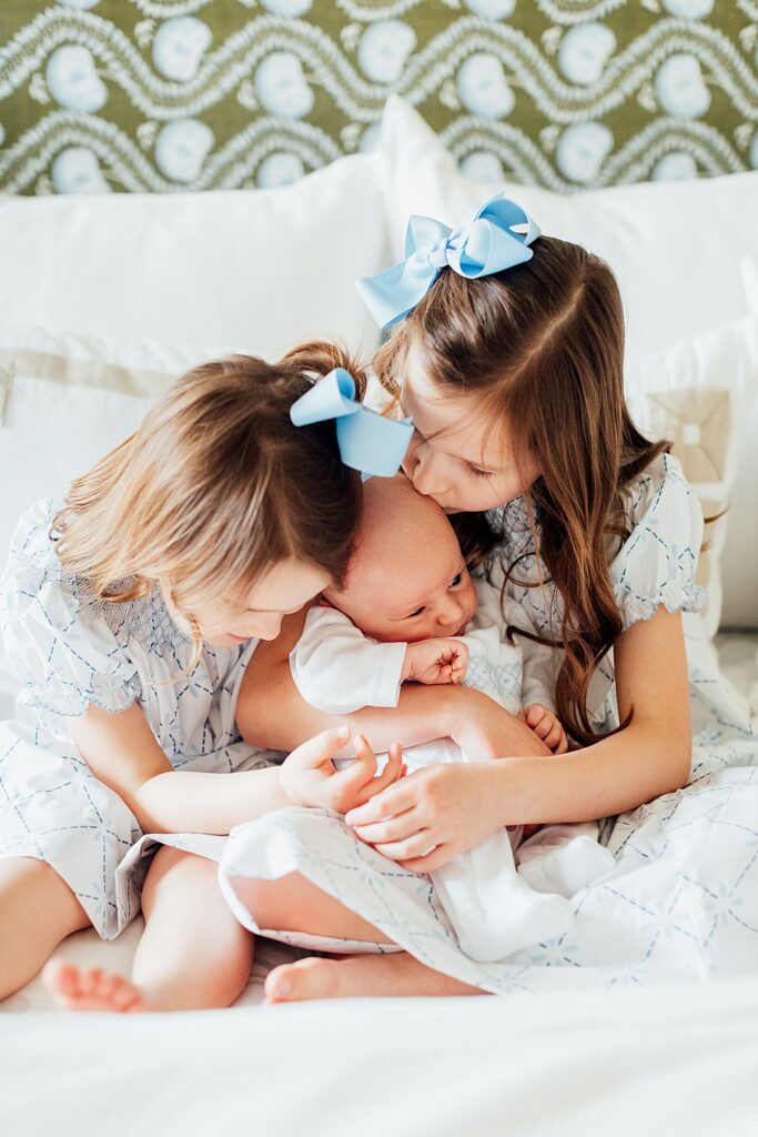 Big sisters snuggling baby boy.